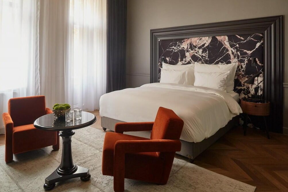 An orange accent chair near the huge bed with white blankets
