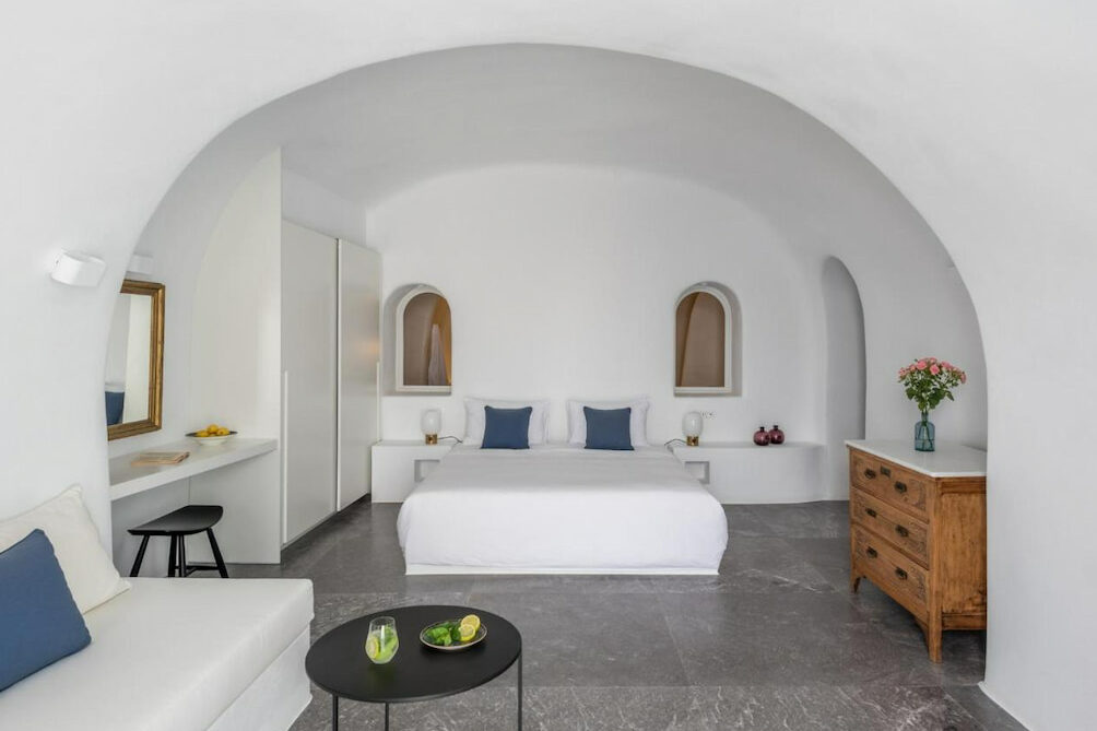 A dome-like luxury room with a comfortable bed with blue pillows with a wooden drawer on the side