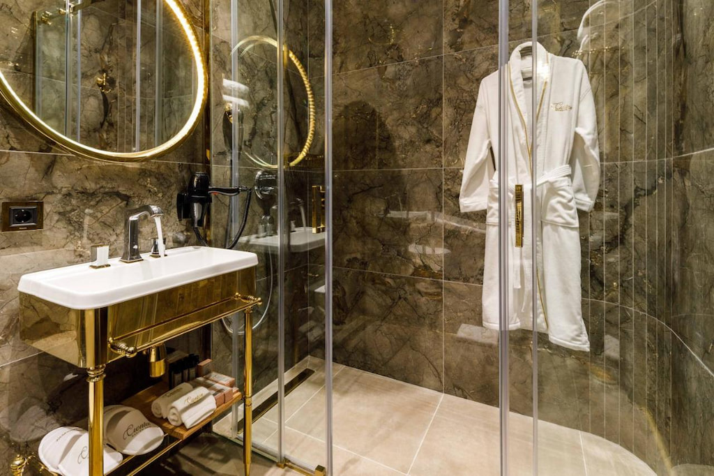 A sophisticated shower area and a white bathrobe hanging is near the gold sink
