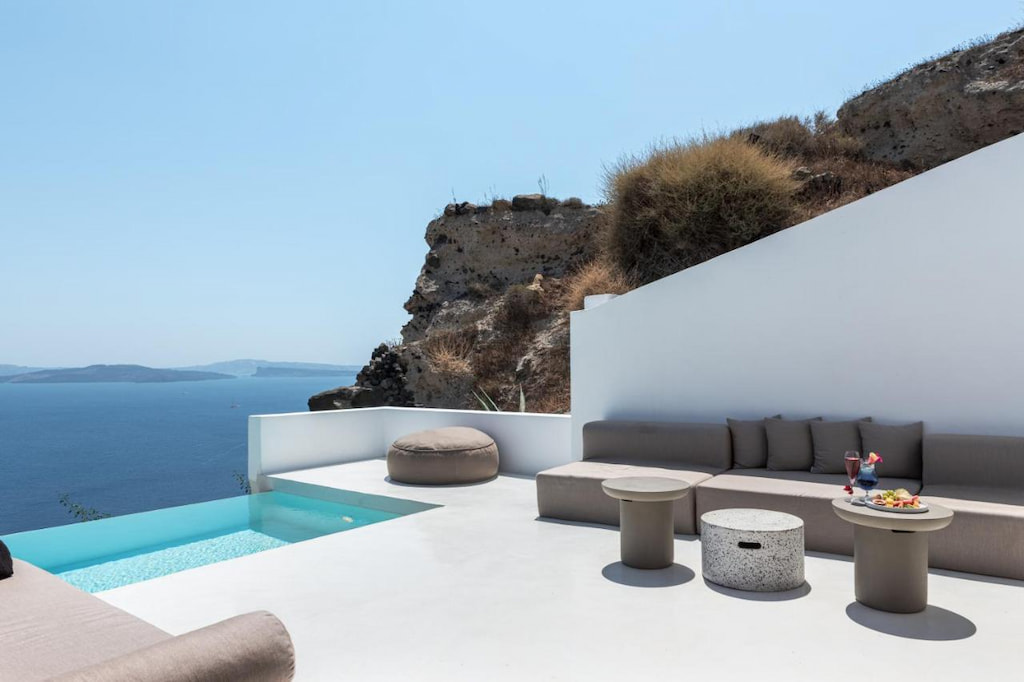 Gray outdoor couches near the table and a bean bag in the corner of the pool deck with the view of the sea