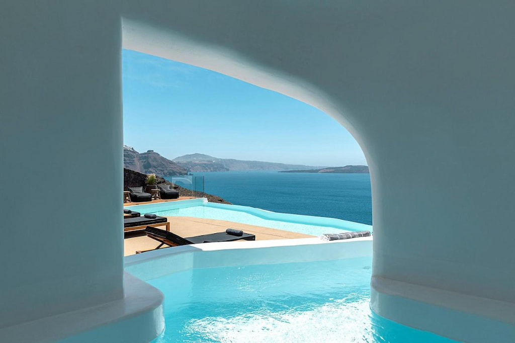 Pool with blue water near the black lounge beds with view of the Aegean Sea