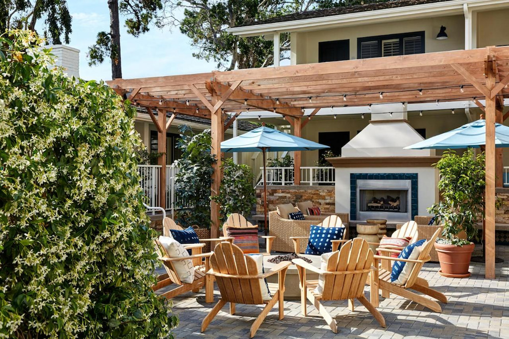 The outdoor area of one of the best Carmel CA hotels with a bonfire area surrounded by wooden chairs, a fireplace, and umbrella shades