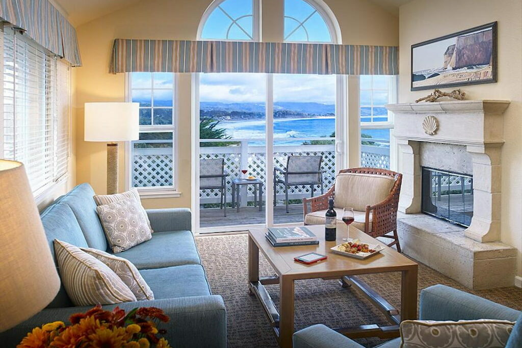 One of the hotels of Half Moon Bay with a cozy sofa set , fireplace and a wooden center table near the balcony and view of the beach.