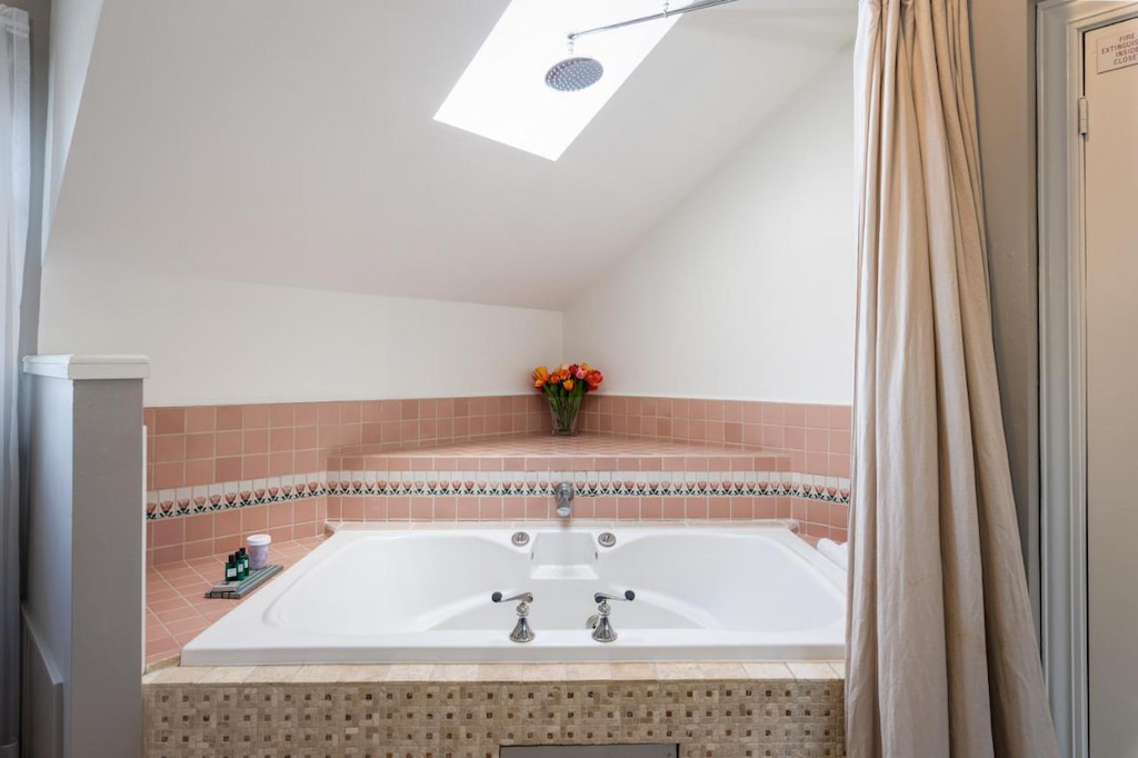 A jacuzzi in the corner of the bathroom with a shower curtain and a ceiling window.