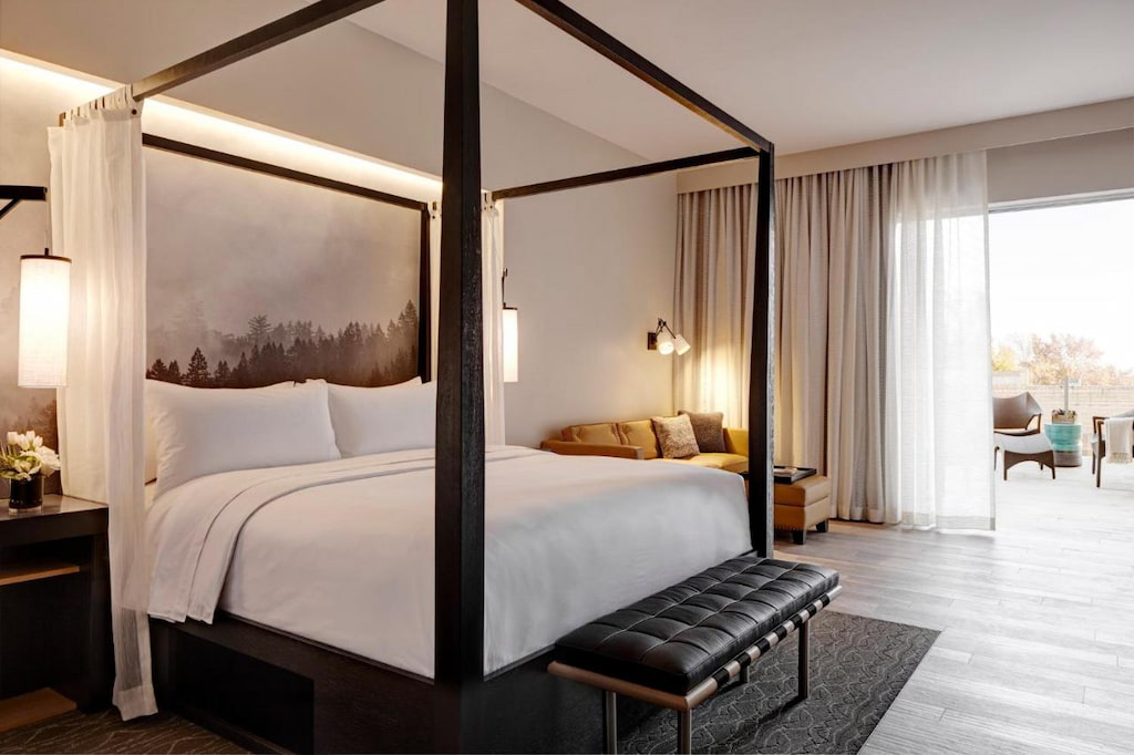 View of one of  the best Napa boutique hotels with a luxurious bed with a black frame and a black bench below it.