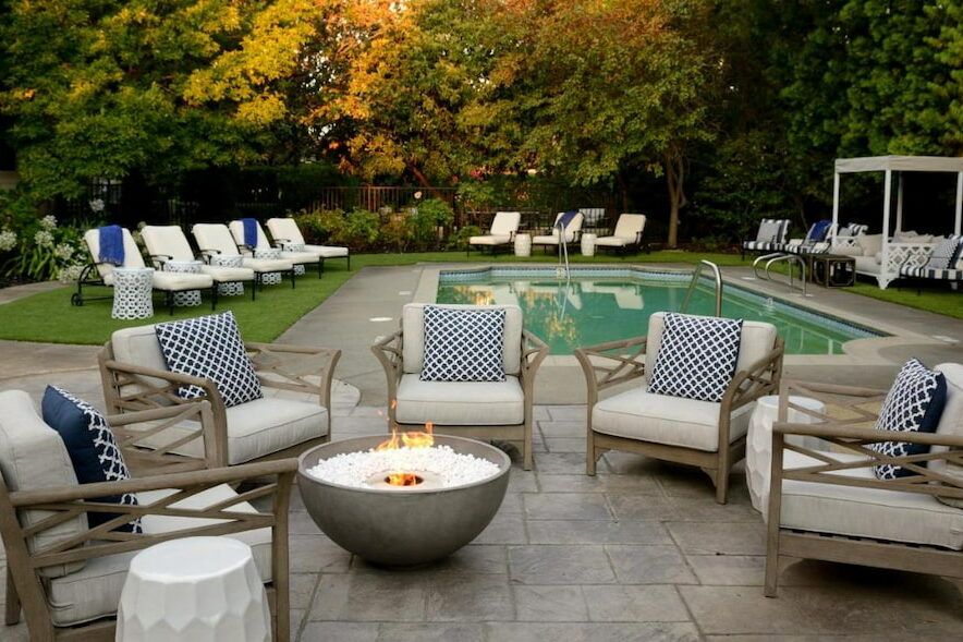 View of the pool area surrounded by pool couches and a modern-style firepit