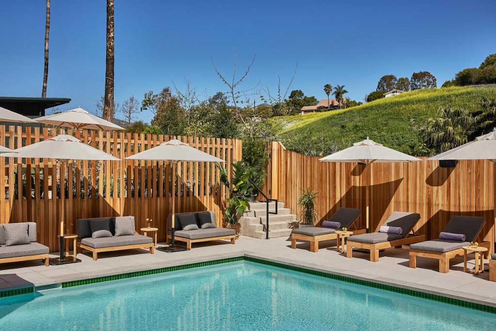 An outdoor swimming pool on the beach hotels Southern California surrounded by a wooden fence, wooden chairs with gray cushions, and umbrella shades
