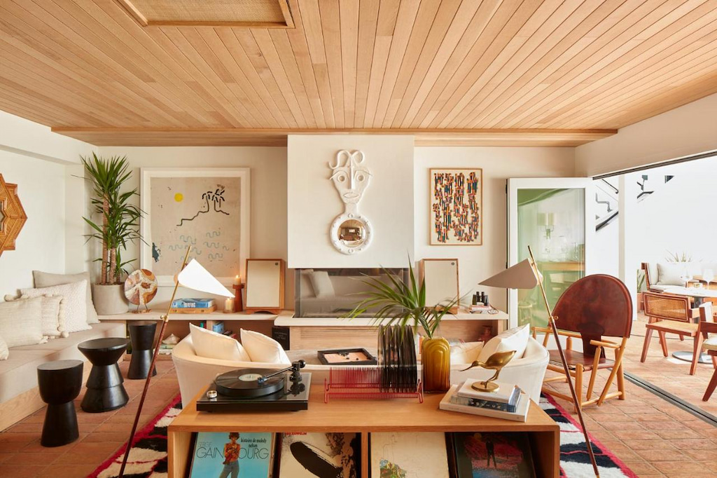 A room in one of the unique Southern California hotels with an artsy room with wooden ceiling, tables, chairs, and couches, decorative art, and records and vinyl player