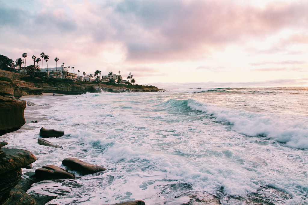 rugged coastline with water, pink and purple sky and palm trees in California sayings
