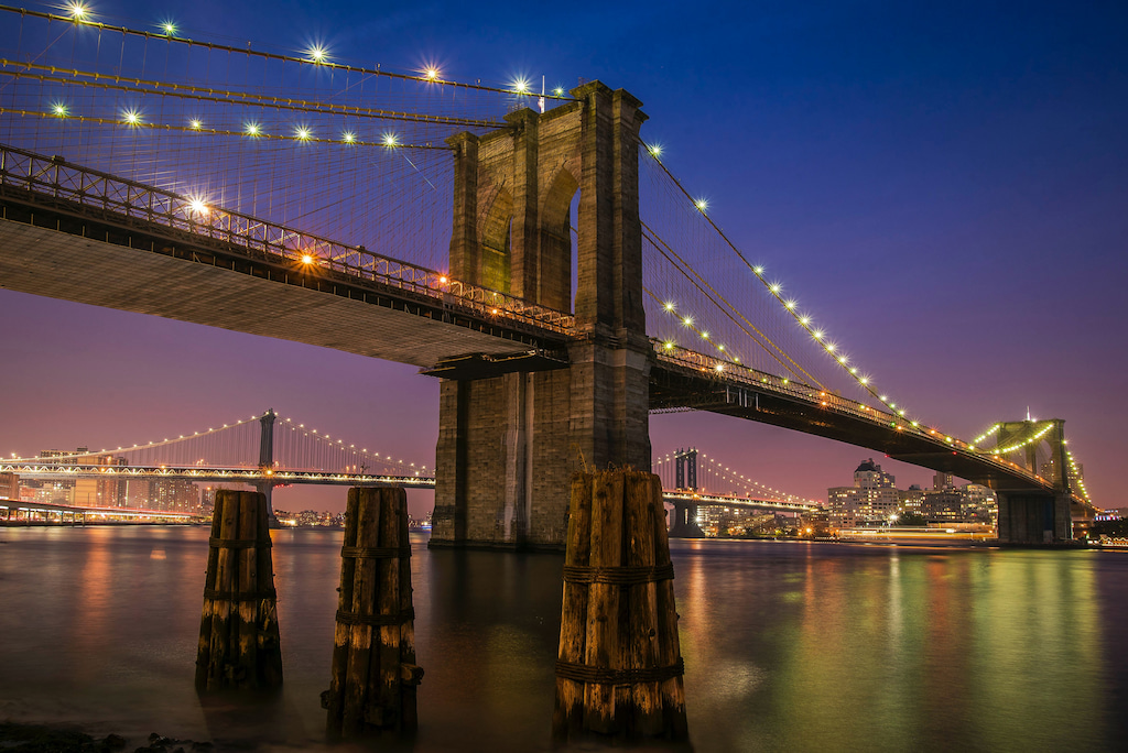 Brooklyn bridge at night all lit up with a purple sky