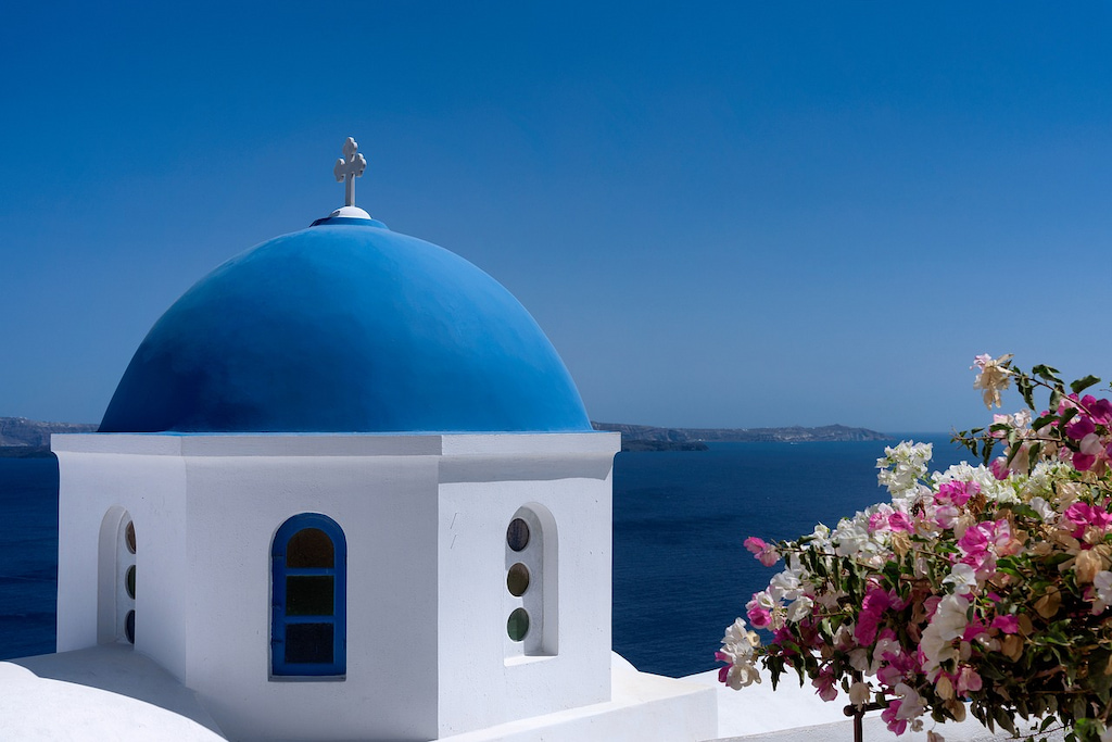 blue domed white building with flowers and ocean in the distance