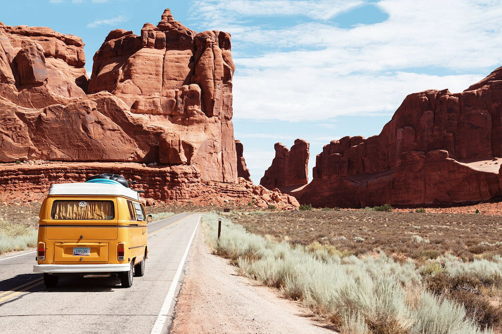 yellow van driving on a road through organic red rocks make a great travel joke