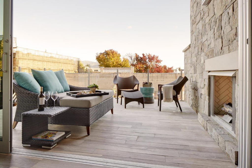 View of an outdoor common area with a couple of padded sofa chairs in fornt of the fireplace.