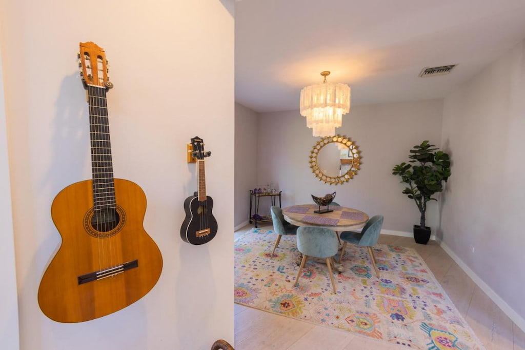 A guitar and ukulele hanging on the wall near the small dining table below the chandelier.