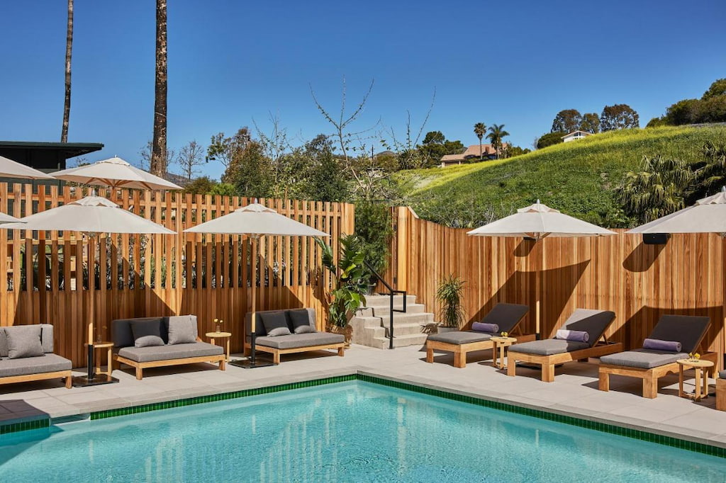 An outdoor pool surrounded by pool benches and umbrellas surrounded by wooden fences.