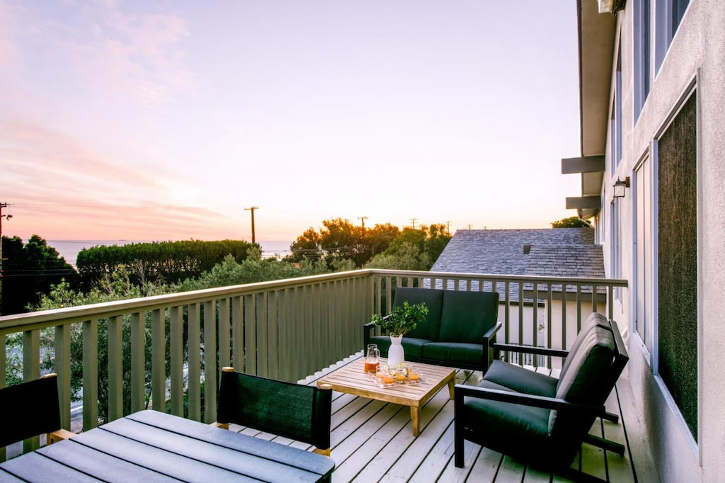 A spacious balcony with black chairs and wooden tables during the sunset.
