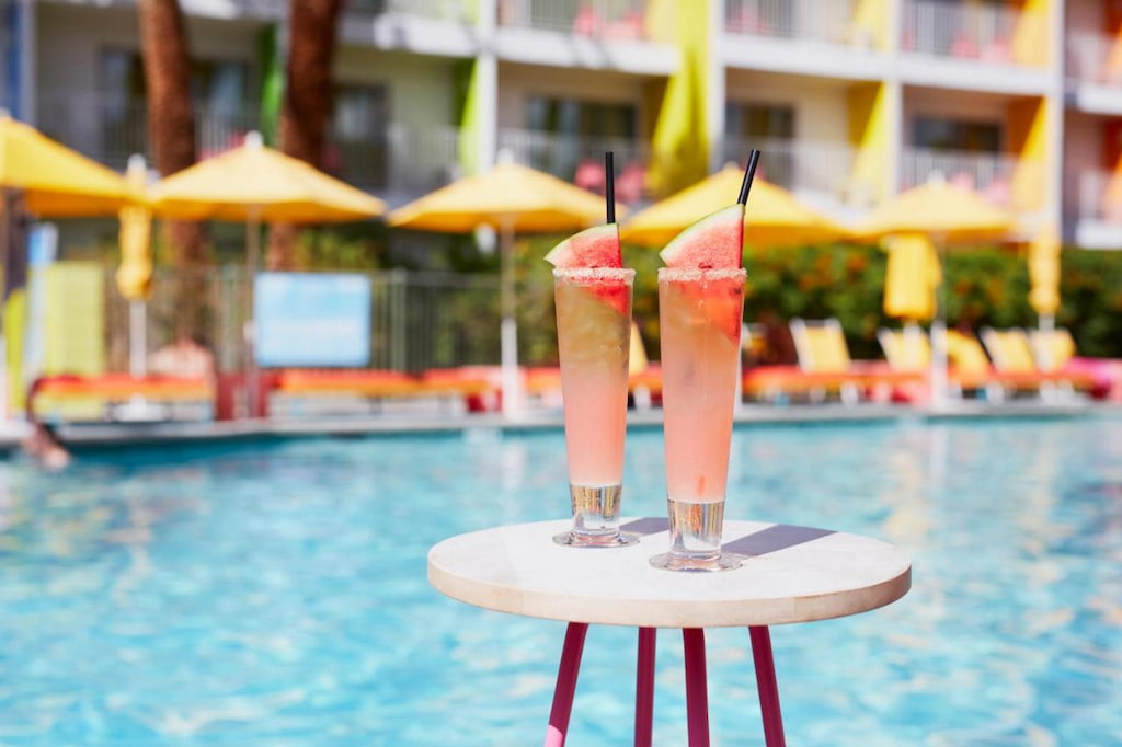 Two watermelon drinks on top of a small round table near the outdoor swimming pool.