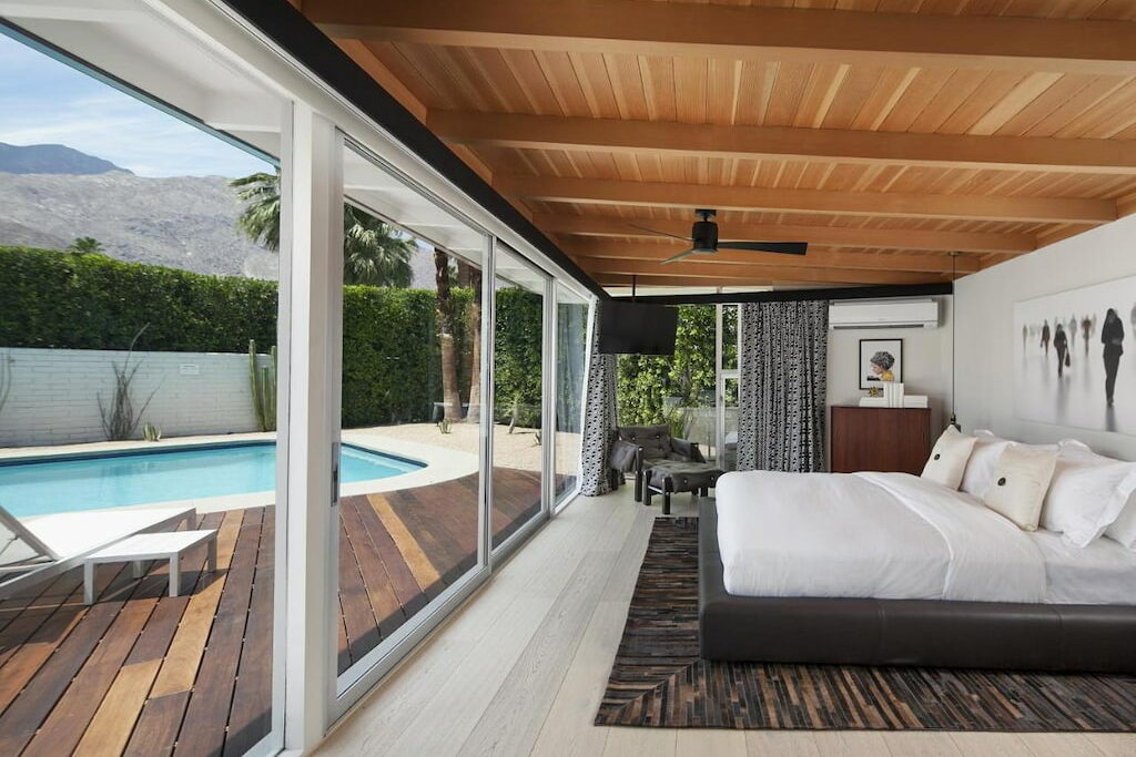 A luxury hotel in Palm Springs, CA with a bed facing the ceiling-to-floor glass windows facing the outdoor pool.