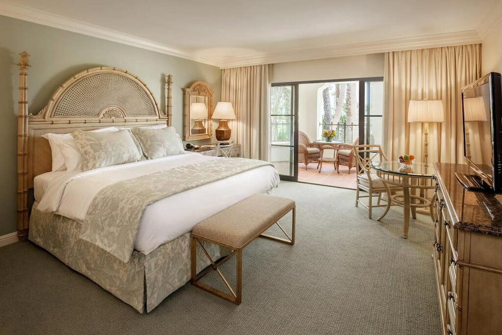 A luxury hotel room in Santa Barbara with a chic bed, bench, tables and chairs near the terrace.