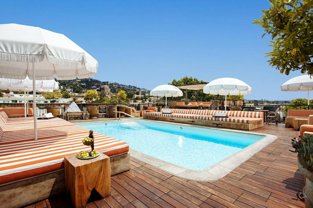 A rooftop pool surrounded by padded benches and umbrellas with an amazing view of the city.
