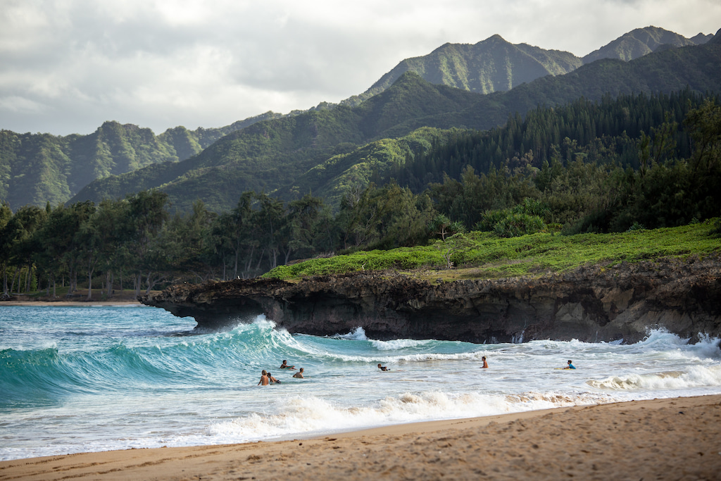 surfers on blue waves with green mountains in the distance