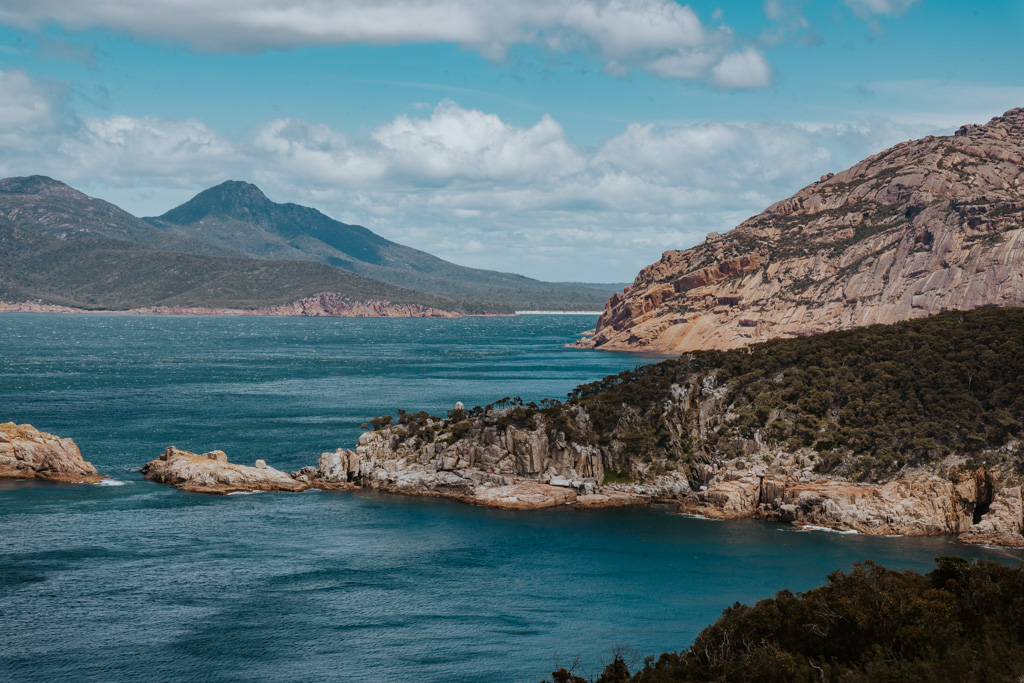 rugged peninsulas of rock covered with low shrubbery jut out into a bright blue ocean inlet in Freycinet National Park one of the best east coast Tasmania attractions