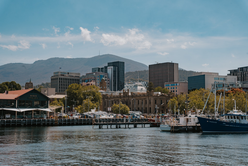 perspective of Hobart harbour with water in the foreground, sail boats moored on docks and modern high rise buildings in the distance