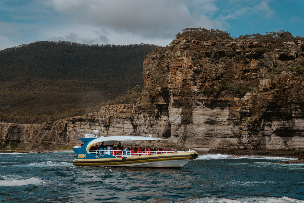 a blue and yellow adventure cruise boat floats in the water on the way to Tasman Island with rocky cliffs in the distance