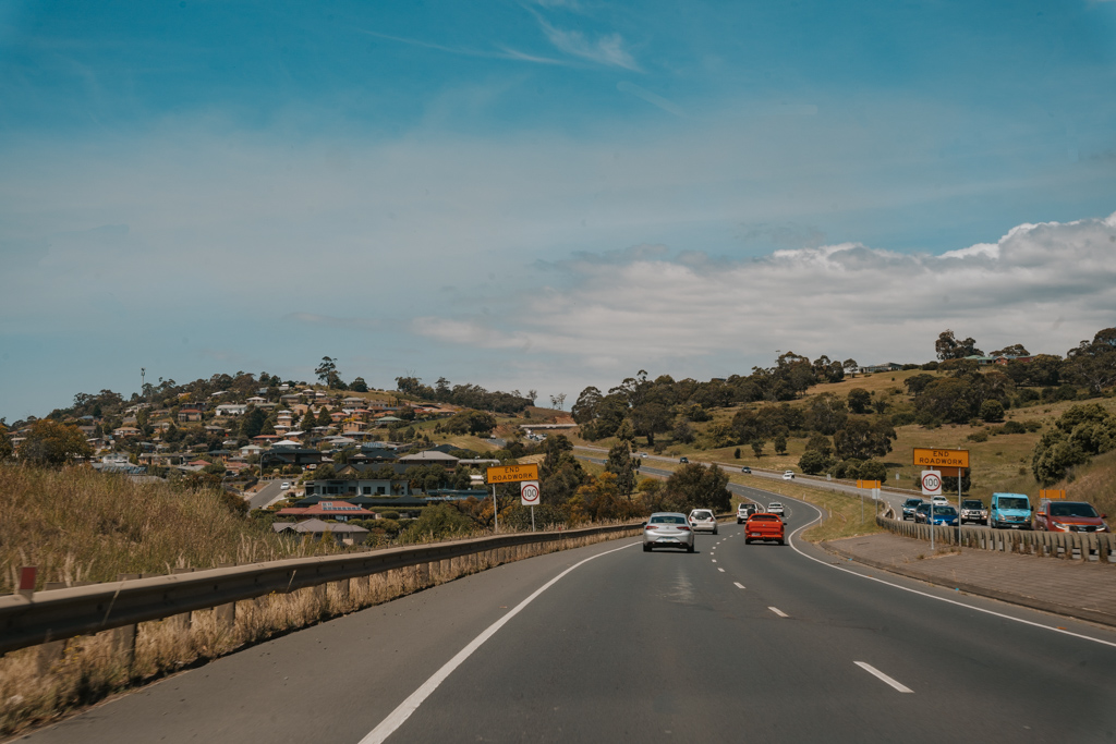 double lane paved road leading toward homes on a rolling green hillside on a Tasmania east coast road trip