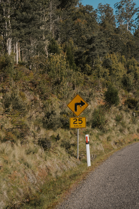 yellow sign indicating a speed limit of your car hire Tasmania to 25 km/h around bends