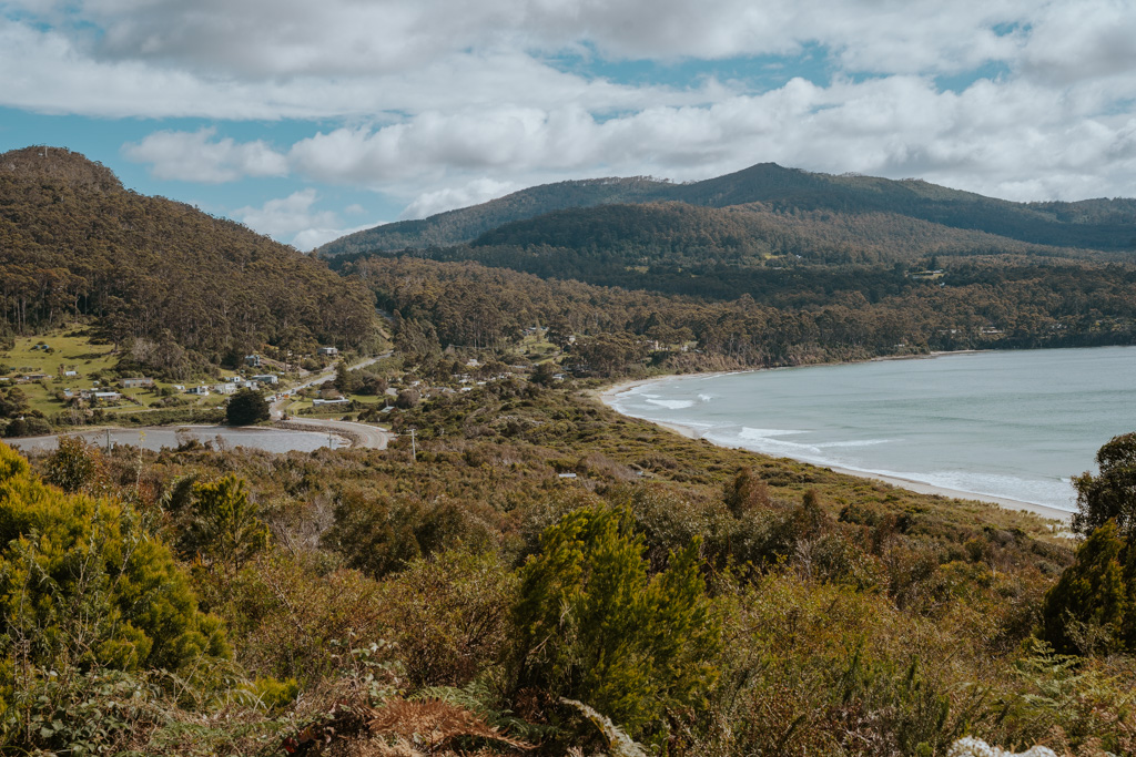 two moon shaped bays back to back connected by a small isthmus of land and dark green mountains a great stop to take with your rental car Tasmania