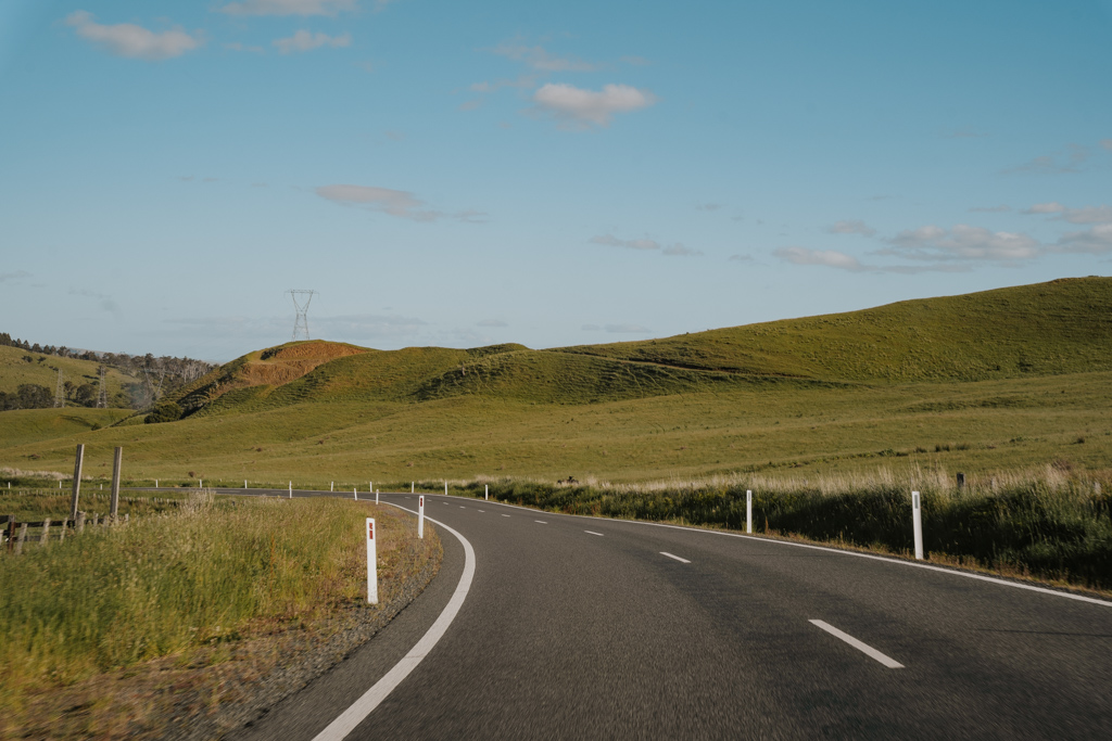 image from the perspective of a car driving on a paved road with hilly green landscape with a blue sky on a road trip in tasmania