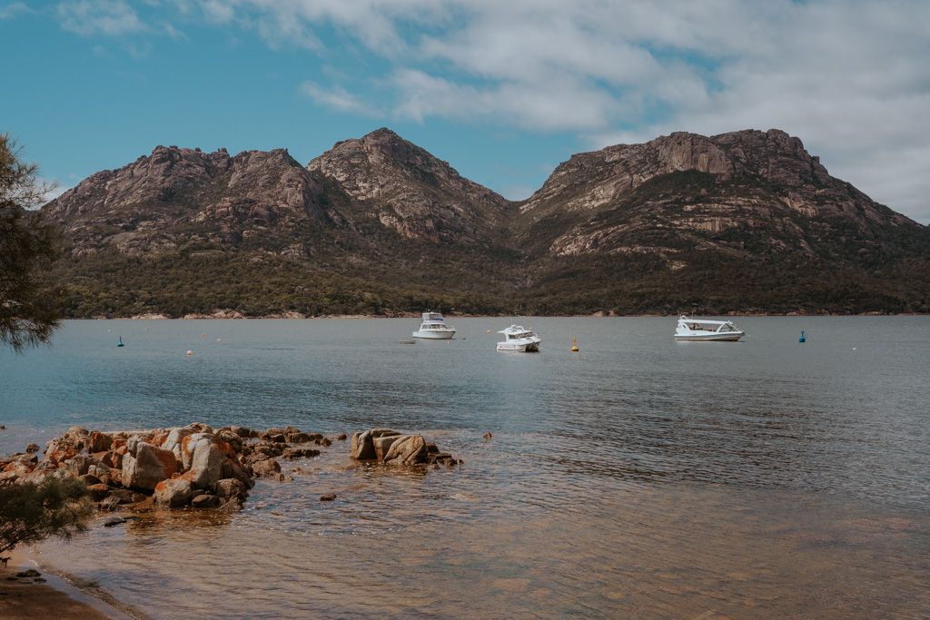 Coles Bay with 3 white boats and large rugged mountains in the background on a lap of Tasmania