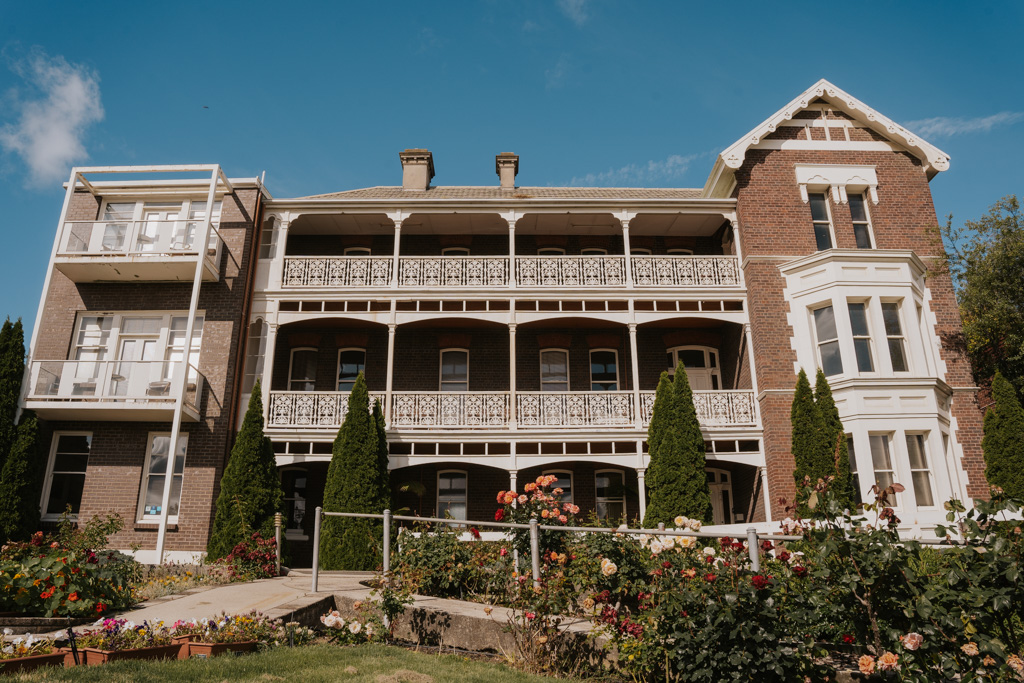 historical three story buildings with red brick and intricate white painted balconies lies behind a rose garden in Launceston