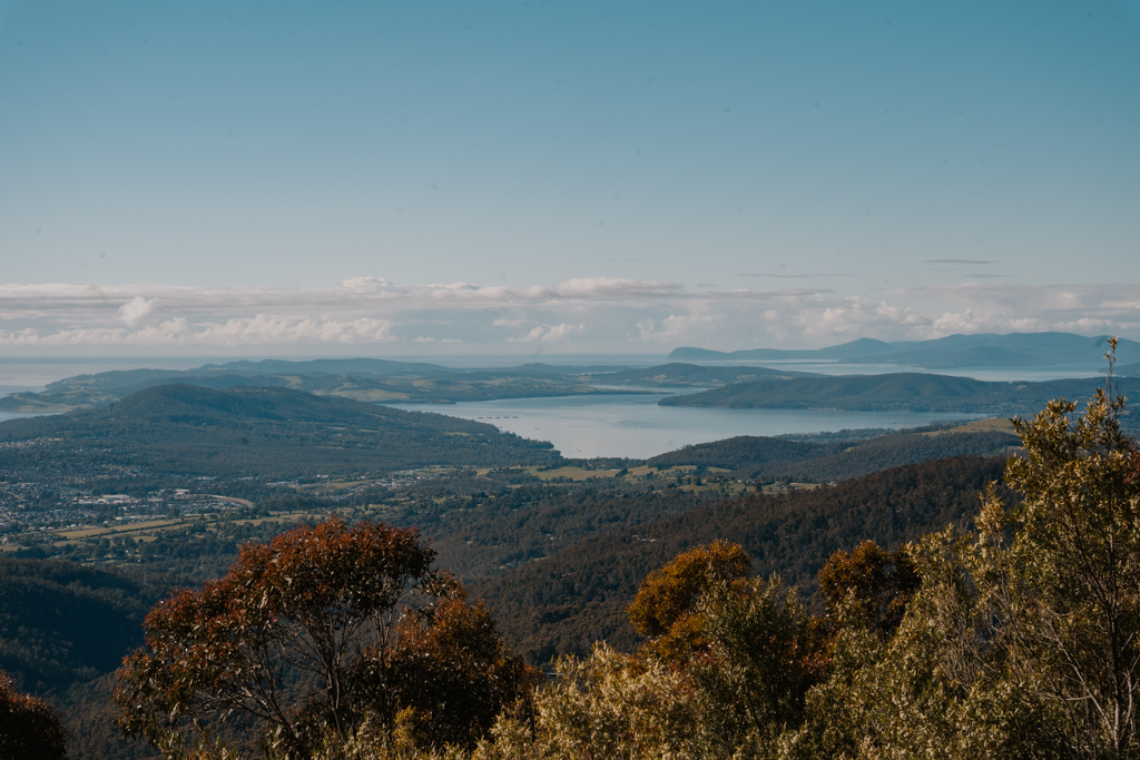a far away panorama of Tasmania's eastern coastline with autumn coloured bushes in the foreground and organic shaped inlets in the distance with blue water