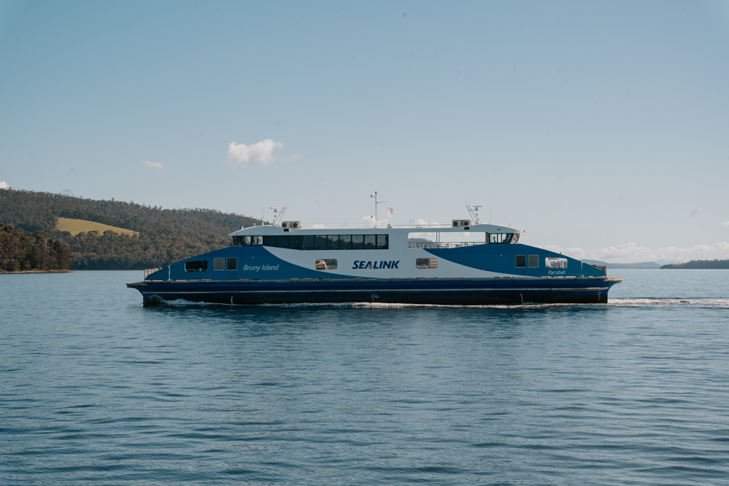 a blue and white passenger ferry with the logo Sealink on the side passes through calm waters on the way from Hobart to Bruny Island
