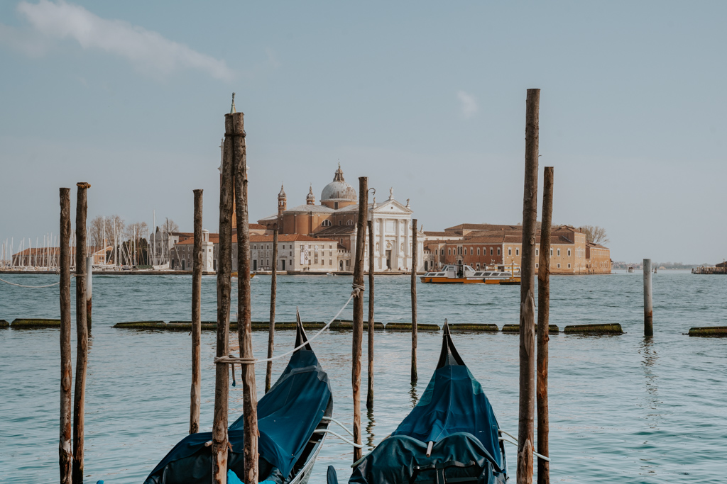 two days in Venice looking out at blue covered gondola boats, wood sticks coming out of the water and historic buildings across the canal in the distance