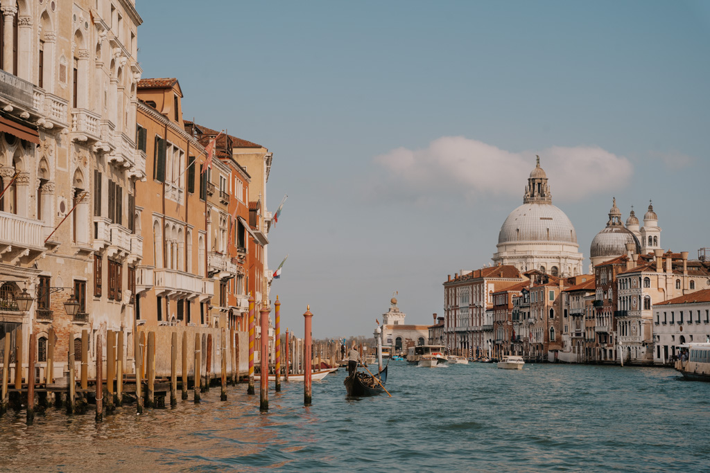 perspective of hotels in Venice with canal view with ornate historic buildings in the distance and gondola on the water on a sunny day
