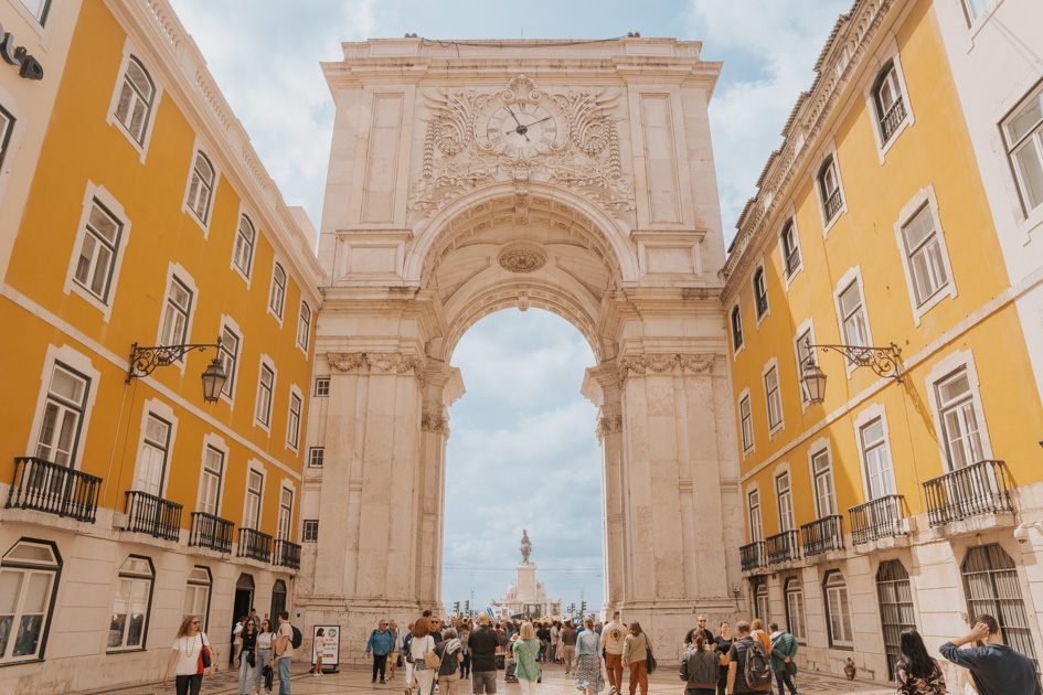 a large white stone arch stands between yellow buildings in Lisbon Portugal the best place to stay in Europe for budget travellers