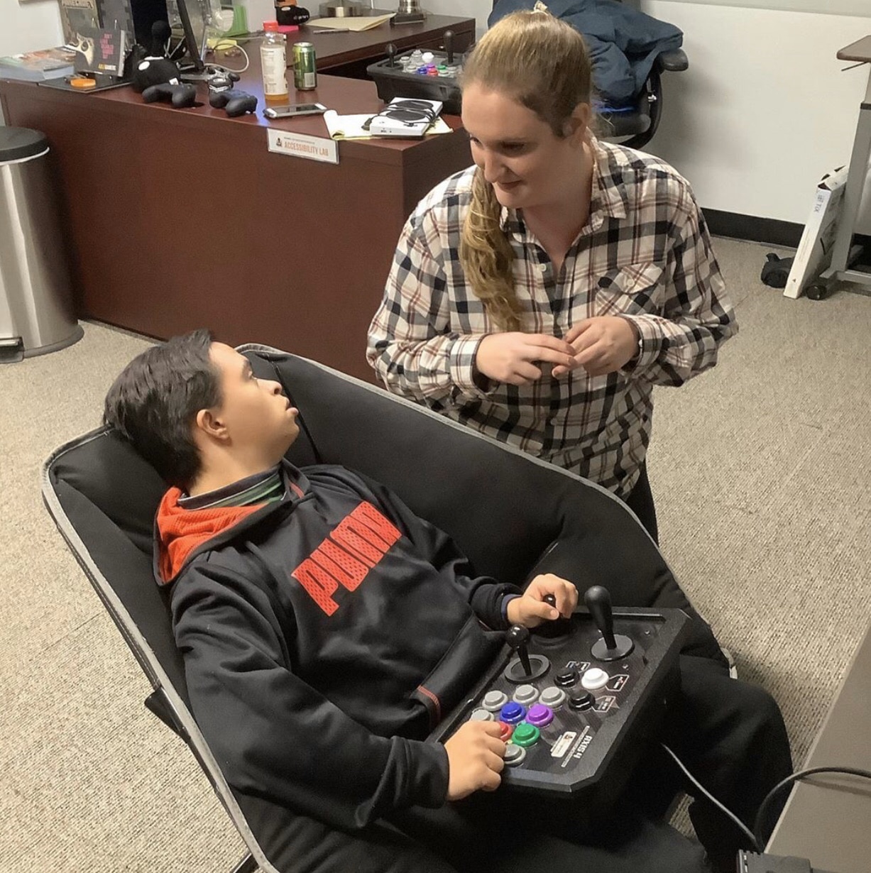Two people, one is gaming using an accessible controller