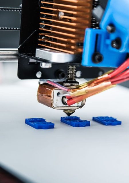 Close up of a 3D printer hotend printing 3 blue parts on the bed of the printer.