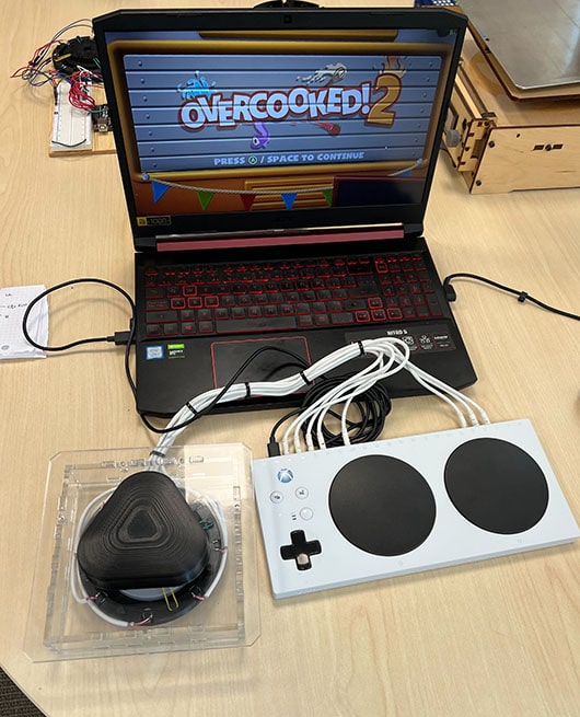 The No Lift No Pull controller sits in front of a laptop with the game Overcooked ready to play. It is connected to an XAC through 8 white wires that feed from the device to the front ports.