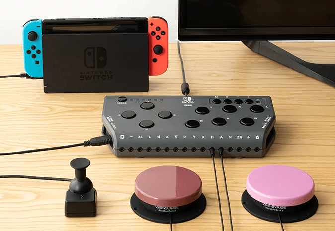  A Hori Flex plugged into a Nintendo Switch. A small joystick, red button, and pink button are all connected and placed in front. 
