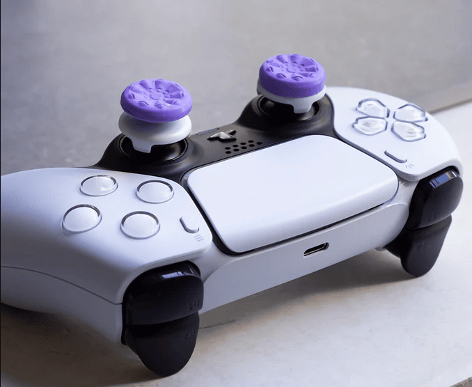 A white PlayStation 5 controller with purple, textured thumb stick toppers. 