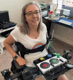 an image of a young woman on a tray in front of here is an adaptive gaming setup with several switches and buttons