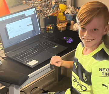 An image of a child smiling using a laptop to game