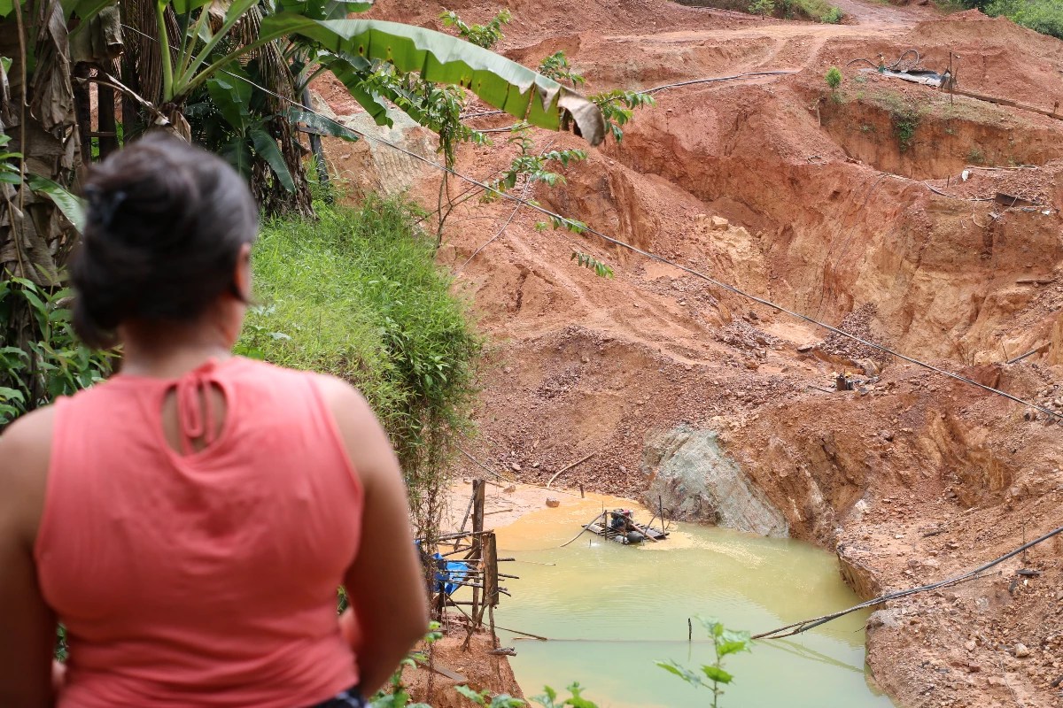 Mulher de 28 anos aparece de costas para a câmera encarando uma imensa área de garimpo