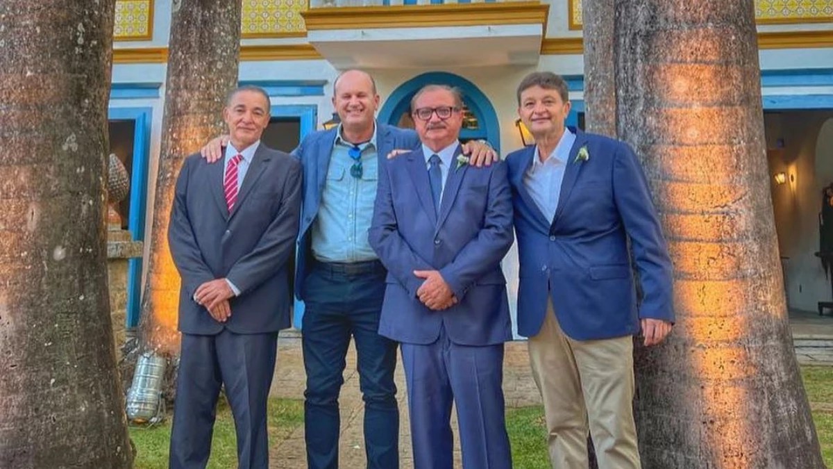 Foto mostra quatro homens brancos na faixa dos 60 anos; ambos vestem terno azul.