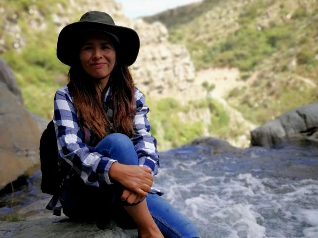 Marlene Quintanilla, pesquisadora da RAISG, é uma mulher branca com cabelos e olhos castanhos. Marlene veste blusa xadrez e chapéu.