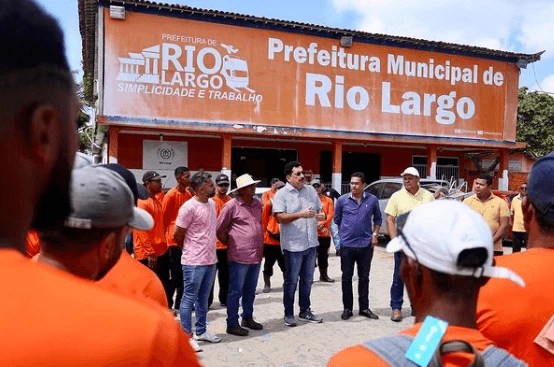 Gilberto Gonçalves, um homem branco de cabelos pretos e bigode, na imagem veste uma camisa azul e calça jeans. Ele discursa em frente à Prefeitura Municipal de Rio Largo.